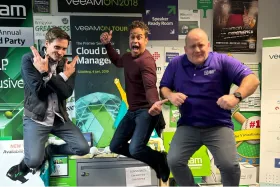 Three men enthusiastically posing in front of a technology-themed exhibition booth, jumping or making dynamic gestures.